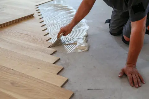 Un operaio stende la colla per posare un nuovo pavimento in legno. Scopri quanto costa rifare il pavimento.