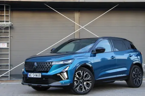 Błękitny Renault Austral 2025 z czarnym dachem i felgami stoi przed szarą, nowoczesną bramą.
