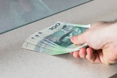 Dłoń przekazuje stos banknotów 100 zł. To przykład, co to depozyt bankowy – pieniądze wpłacane do banku.