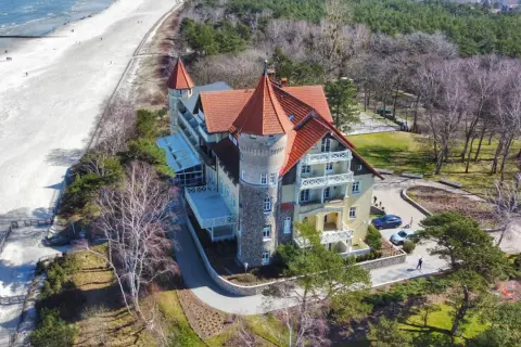 Elegancki budynek z czerwoną dachem i wieżą, blisko piaszczystej plaży i morza.