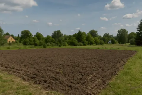 Przekształcenie działki budowlanej na rolną: świeżo zaorane pole z domem w tle.