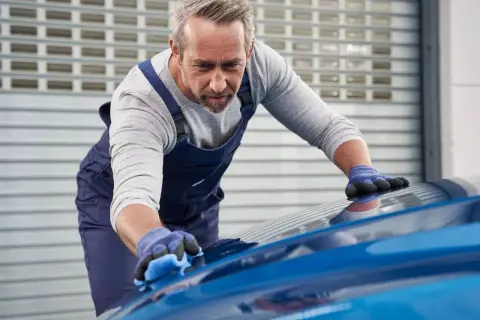 Un esperto opera la verniciatura auto con cura, lucidando la carrozzeria blu brillante.