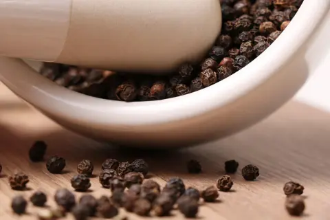 Schwarze Pfefferkörner in einem Mörser. Sie stammen ursprünglich aus Indien und sind ein beliebtes Gewürz.