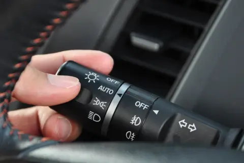 Dłoń reguluje przełącznik świateł: AUTO, światła mijania, światła dzienne.