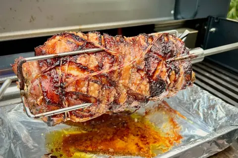 Ein saftiges, am Spieß gebratenes Stück Fleisch, das nach Porchetta aussieht, tropft in eine Aluschale.