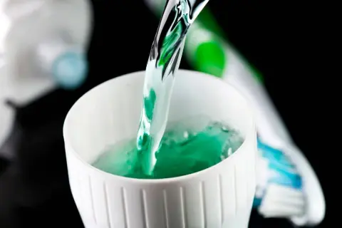 Enjuague bucal verde vertiéndose en un vaso blanco, parte de la rutina de fluorización dental en adultos.