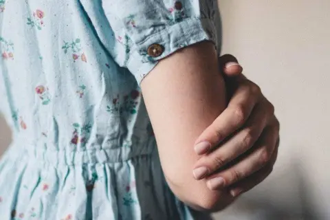 Een vrouw in een bloemenjurk houdt haar arm vast, misschien om oefeningen tegen trillende handen te doen.