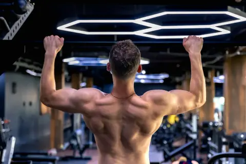 Mężczyzna wykonuje ćwiczenie scapular pull ups na drążku, budując silne plecy i ramiona w nowoczesnej siłowni.