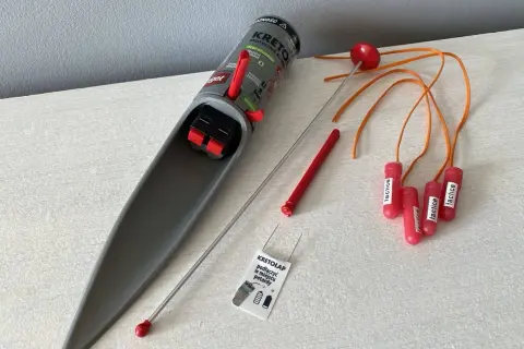 Pułapka na krety z mechanizmem spustowym i kilkoma czerwonymi "petardami" z pomarańczowymi linkami.