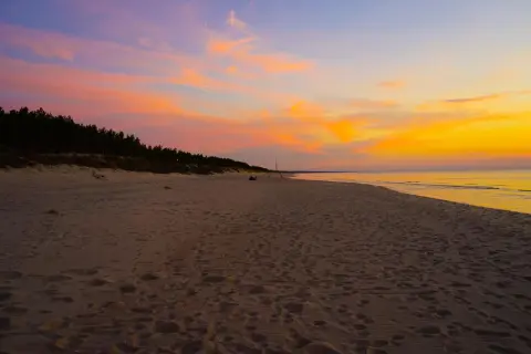 Piękny zachód słońca nad morzem. Niebo mieni się odcieniami różu i pomarańczy, a plaża jest pusta, tylko ślady stóp przypominają o minionych spacerach.