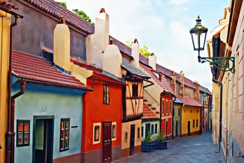 Kolorowa, wąska uliczka w Pradze, znana jako Złota Uliczka, z malowniczymi, ciasno zabudowanymi domkami i zabytkową latarnią.