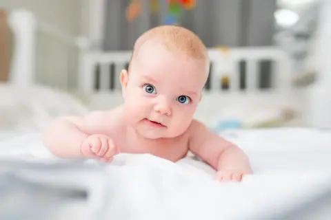 Niebieskooki, 3-miesięczny maluch leży na brzuchu, ćwicząc mięśnie szyi.