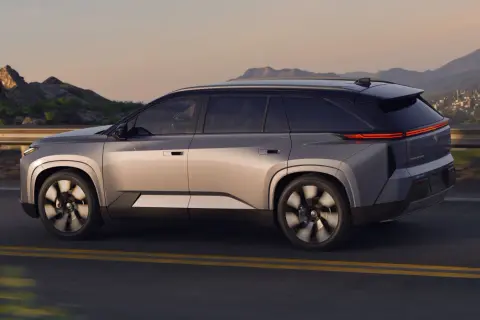 Srebrny Toyota Highlander jedzie po drodze z górzystym krajobrazem w tle. Sprawdź aktualną toyota highlander cena!
