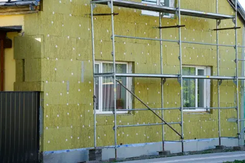 Lavori in corso per pulire muro esterno con cappotto isolante. L'edificio è circondato da ponteggi metallici.