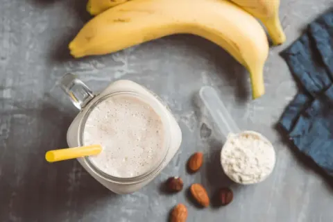 Ein cremiger Proteinshake mit Banane und Nüssen, daneben eine Schaufel Proteinpulver, bereit für das Training. Kreatin im Proteinshake für mehr Power.