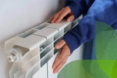 Mani che toccano un termosifone bianco, suggerendo come svuotare un termosifone per la manutenzione.