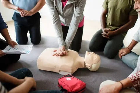 Persone in cerchio praticano RCP su un manichino. Si impara da chi sono designati gli addetti al primo soccorso.
