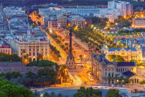 Vista aerea di Barcellona di notte, con la Rambla illuminata, palme e locali notturni che brillano.