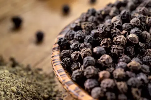 Schwarze Pfefferkörner in einer Holzschale, daneben gemahlener Pfeffer. So wird Pfeffer hergestellt: Ernte, Trocknung und Mahlung.