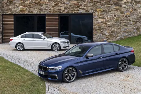 Dwa BMW, jeden granatowy, drugi biały, przed nowoczesnym budynkiem. Czy to xdrive co to za napęd?
