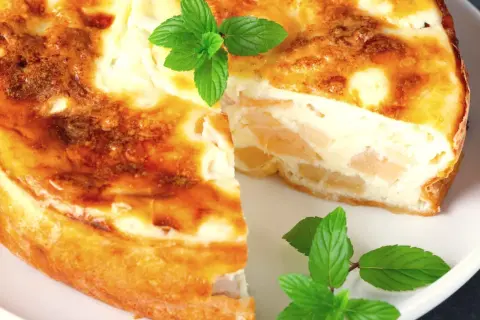 Pyszne ciasto z serka wiejskiego z kawałkami owoców, ozdobione listkami mięty.