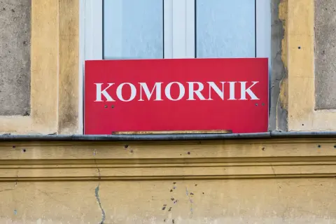 Czerwony szyld z napisem "KOMORNIK" nad oknem. Może to oznaczać, że komornik sądowy działa w tym miejscu, a kwota wolna od zajęcia jest chroniona.
