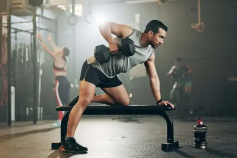 Mann mit shredded body trainiert im Fitnessstudio mit Hanteln.