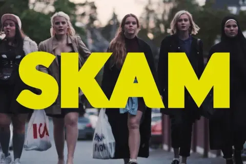Fem tjejer går längs en gata, med den stora gula texten "SKAM" över bilden. En av dem dricker ur en flaska.