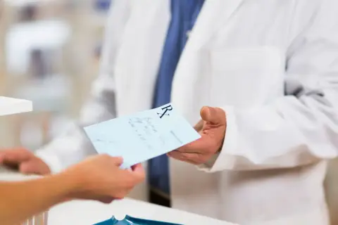 Farmaceuta w białym fartuchu podaje receptę. Dowiedz się, jak odzyskać kod recepty, aby zrealizować leki.