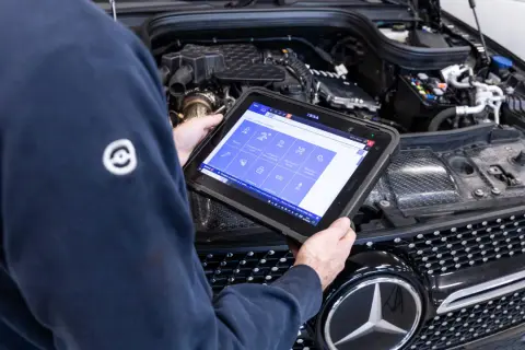 Tecnico esegue la revisione auto con tablet diagnostico, controllando i sistemi del motore.