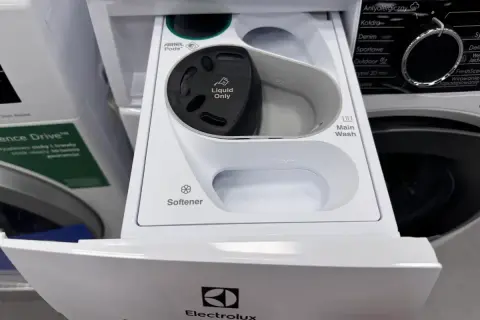 Szara przegródka na detergenty w pralce Electrolux ładowanej od góry. Widać miejsce na kapsułki Ariel, płyn do płukania i pranie główne.