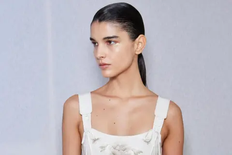 Mujer con coleta alta lisa, maquillaje sutil y vestido blanco bordado.