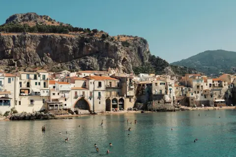 Un incantevole borgo da visitare in Sicilia, con case color pastello affacciate sul mare azzurro e una scogliera imponente alle spalle.