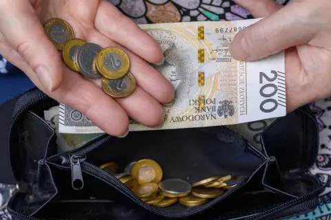 Dłonie trzymające polskie banknoty i monety nad otwartym portfelem.