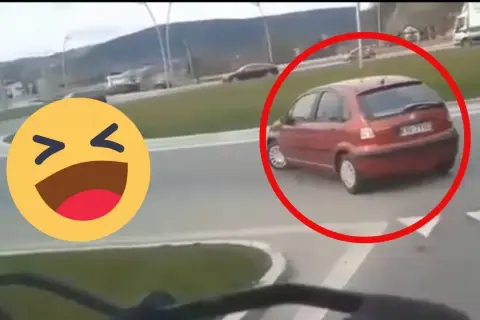 Czerwony samochód próbuje zawrócić na rondzie, ale robi to na lewo, co wygląda na niezbyt przemyślane. Obok śmieje się emotikon.