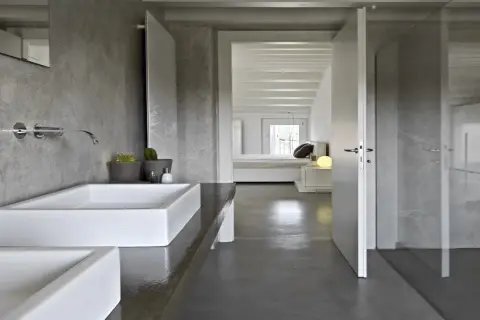 Salle de bain moderne avec murs en béton ciré, lavabos rectangulaires blancs et douche vitrée. La résine salle de bain offre un aspect brut et contemporain.