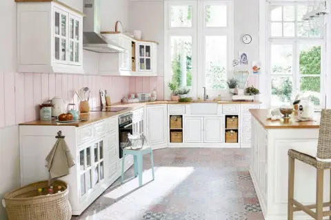 Une cuisine campagne chic lumineuse avec des meubles blancs, un plan de travail en bois, un carrelage coloré et de grandes fenêtres donnant sur le jardin.