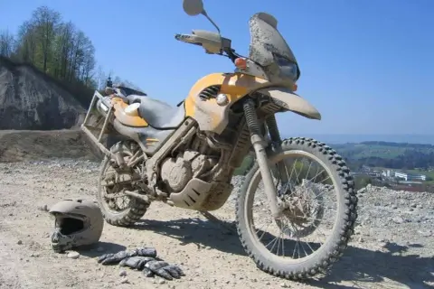 Żółty motocykl po off-roadowej przygodzie, pokryty błotem. Obok leżą kask i rękawice. Idealny do lekkiego enduro.