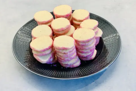 En hög med hembakade brysselkex med rosa sockerkanter ligger på en mörk tallrik. Perfekt för fikat!