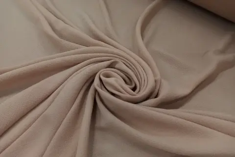 Delikatna, beżowa żorżeta układa się w miękkie fałdy, tworząc elegancką spiralę.