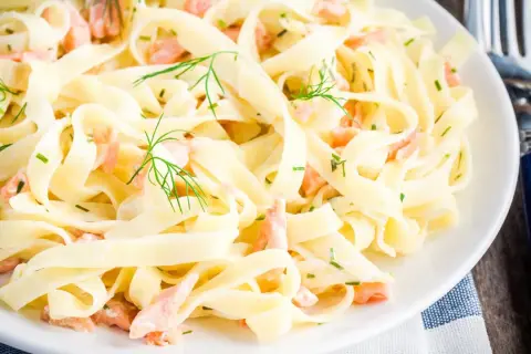 Tagliatelle mit Lachs, garniert mit Dill und Schnittlauch, auf einem weißen Teller. Ein köstliches Gericht, das zum Genießen einlädt.