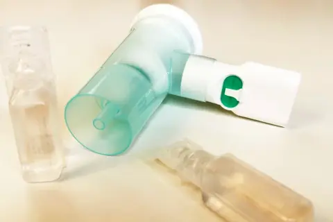 Nebulizator z zielonym przyciskiem i ampułkami, jedna z nich zawiera roztwór NaCl 0,9%.