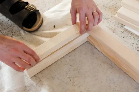 Ręce składają drewniane elementy, by stworzyć ramę ławki. To początek projektu jak zrobić ławkę DIY.