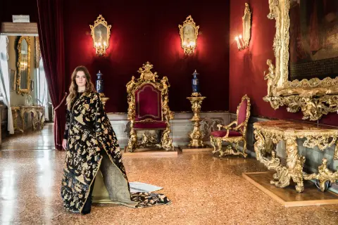 Donna con abito prezioso in una sala dorata, un'elegante tessitura Bevilacqua per una visita regale.