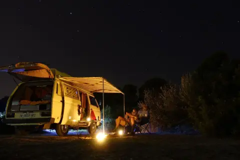 Sternenhimmel über einem Campervan mit ausgefahrener Markise. Ein Paar sitzt davor, die perfekte Mallorca Route für Camper.