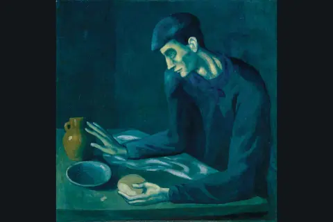 A man in a cap, characteristic of Picasso's Blue Period, sits at a table with a jug and bread, his face illuminated by a somber, blue light.