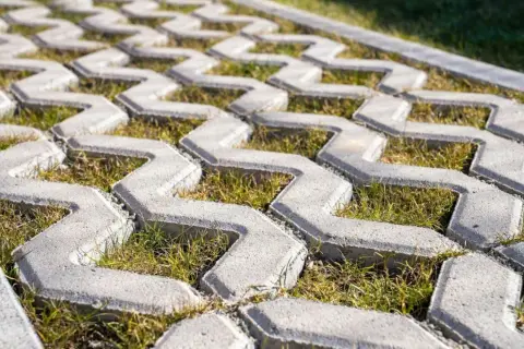 Jak siać trawę w płyty ażurowe? Widok z bliska na betonowe płyty z przestrzeniami wypełnionymi zieloną trawą.