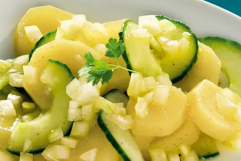 Ein appetitlicher Kartoffelsalat mit Gurken, verfeinert mit Zwiebeln und Petersilie.