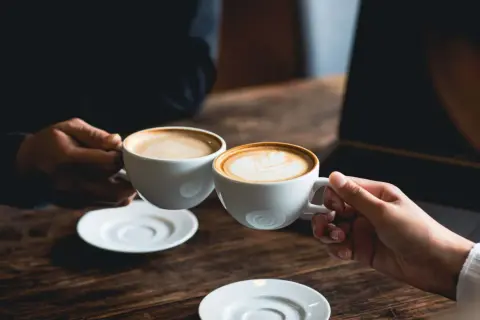 Dos tazas de café humeante, una con arte latte. El café es bueno para la concentración y el disfrute.