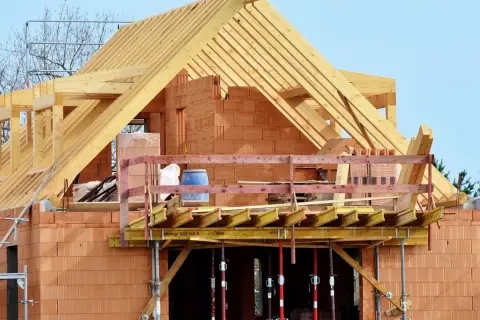 Budowa domu z cegły, widoczna drewniana konstrukcja dachu i balkon. Dopuszczalny błąd wymiarów budynku jest tu nieistotny, liczy się postęp prac.